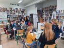 Zdjęcie przedstawia osoby grające w gry planszowe podczas cotygodniowych spotkań integracyjnych w Bibliotece.