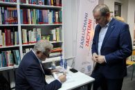 Zdjęcie przedstawiające 2 Panów jeden podpisuje książkę
