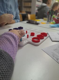 Zdjęcie przedstawia grających w grę planszową w bibliotece.