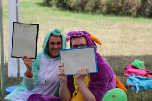 Pracownicy biblioteki w przebraniu jednorożca i smoka, pokazują swoje wersje wyturlanych kotków