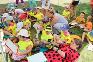 Dzieci siedzą na trawie i rysują kotki w zabawie wyturlaj kotka