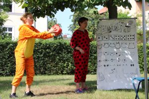 Bibliotekarki w strojach tygrysa, który trzyma dużą kostkę do gry i biedronki, koło planszy, tłumaczą zasady zabawy wyturlaj kotka