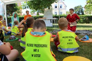 Dzieci siedzą na trawie i słuchają wiersza