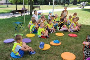 Dzieci siedzą na trawie i słuchają wierszyka