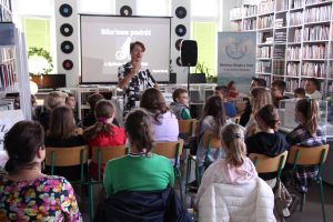 Zdjęcie przedstawia stojącego mężczyznę, który opowiada. Młodzież siedząca na krzesłach słucha.