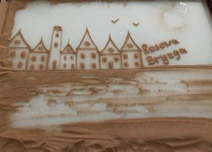 Zdjęcie na którym widzimy starą rybacką osadę, mewy oraz napis Bryzga Rosowa wszystko usypane z piasku 