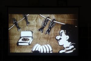 Zdjęcie na którym widzimy suszące się ryby, twarz kupca z sumiastym wąsem wszystko usypane z piasku 