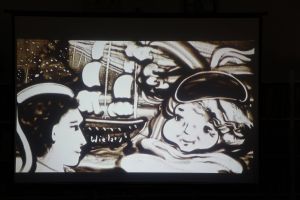 Zdjęcie na którym widzimy twarz staruszki oraz jej syna, w tle bryg wieloryb wszystko usypane z piasku