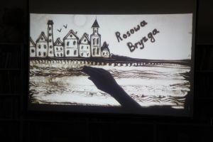 Zdjęcie na którym widzimy starą rybacką osadę, mewy oraz napis Bryzga Rosowa wszystko usypane z piasku