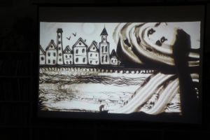 Zdjęcie na którym widzimy starą rybacką osadę, mewy oraz napis Bryzga Rosowa wszystko usypane z piasku 