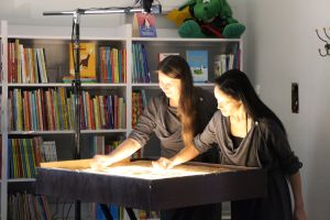 Zdjęcie dwóch pań artystek usypujących z piasku kolejne obrazy historii