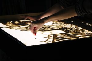 Zdjęcie na którym widzimy ręce artyski tworzące kolejne piaskowe obrazy