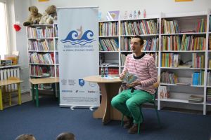 Zdjęcie przedstawia mężczyznę w Bibliotece. Siedzi na krześle i trzyma książkę.