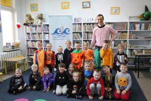 Zdjęcie przedstawia grupę dzieci i osobę dorosłą w Bibliotece.