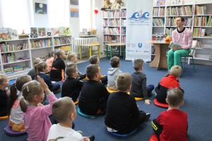 Zdjęcie przedstawia grupę dzieci i osobę dorosłą w Bibliotece.