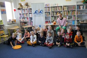 Zdjęcie przedstawia grupę dzieci i osobę dorosłą w Bibliotece.