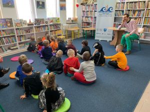 Zdjęcie przedstawia grupę dzieci i osobę dorosłą w Bibliotece.