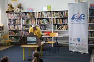 Zdjęcie przedstawia kobietę w Bibliotece. Kobieta pochyla się nad drewnianym teatrzykiem