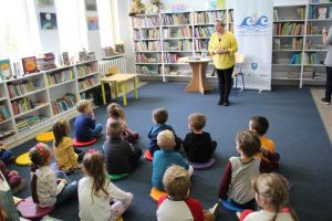 Zdjęcie przedstawia grupę dzieci i osobę dorosłą w Bibliotece.