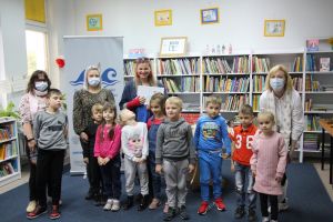 Zdjęcie przedstawia grupę dzieci i osoby dorosłe w Bibliotece.